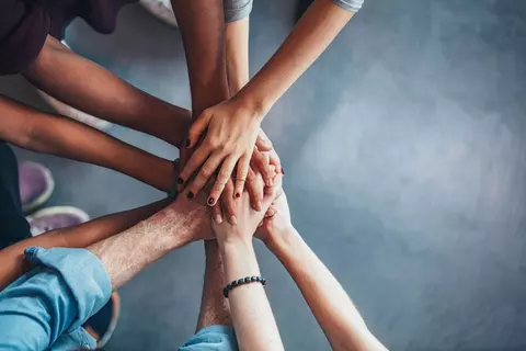 Várias pessoas com as mãos juntas ao meio em sinal de colaboração
